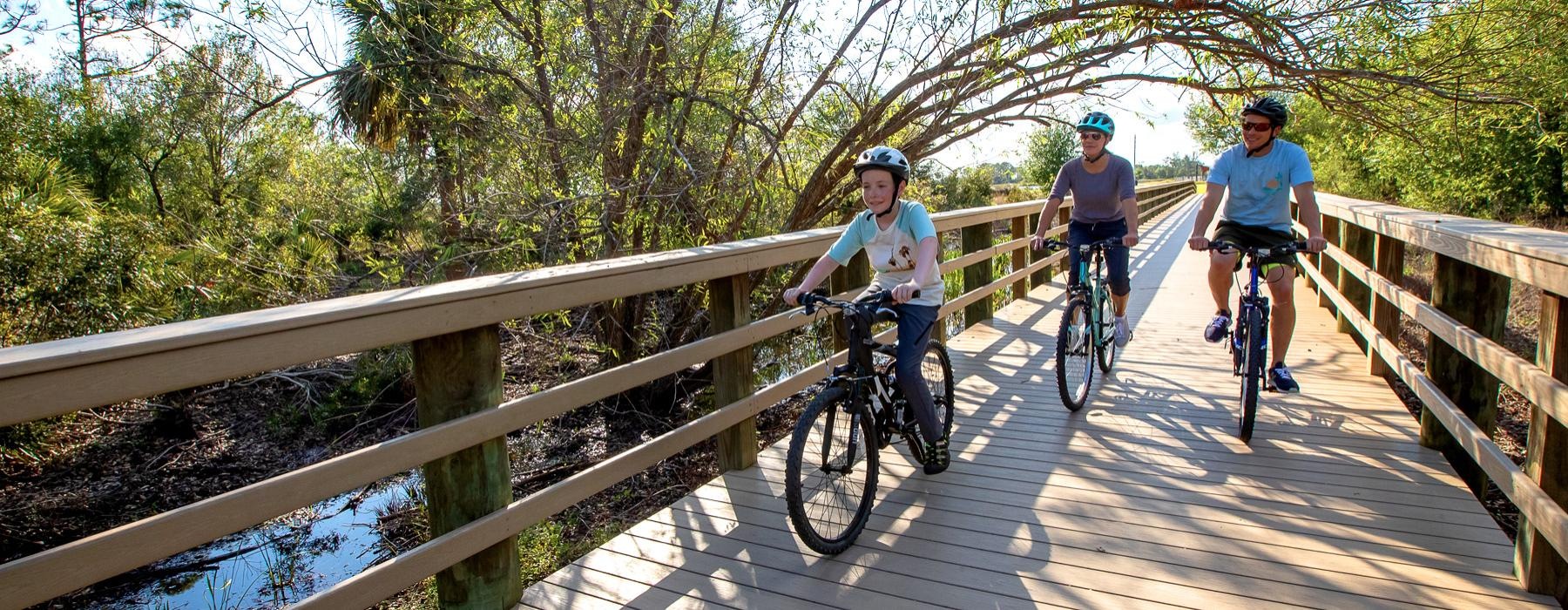 a family riding their bicycles across a wooden park bridge